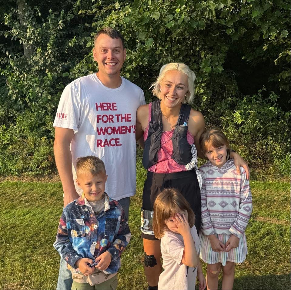 A runner stands outdoors with her husband and three children after an endurance race.