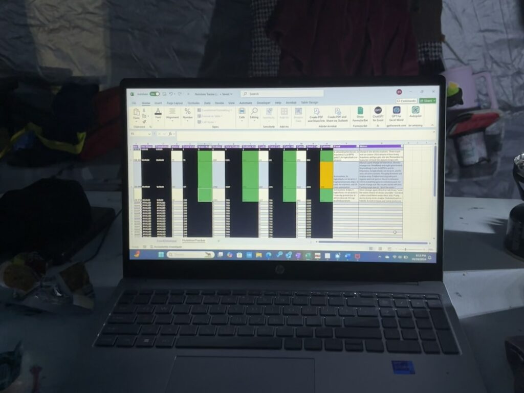 A laptop inside a race tent displays a detailed nutrition-tracking spreadsheet with color-coded columns for hydration, sodium, carbohydrates, calories, caffeine, food, and notes.